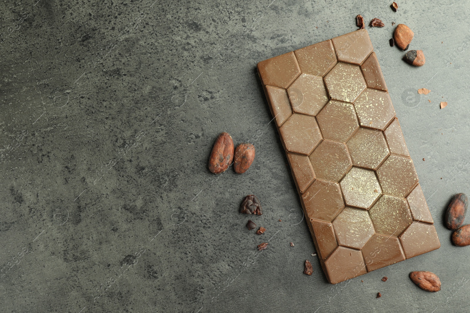 Photo of Tasty Dubai chocolate with pistachio, knafeh and cocoa beans on grey textured table, flat lay. Space for text