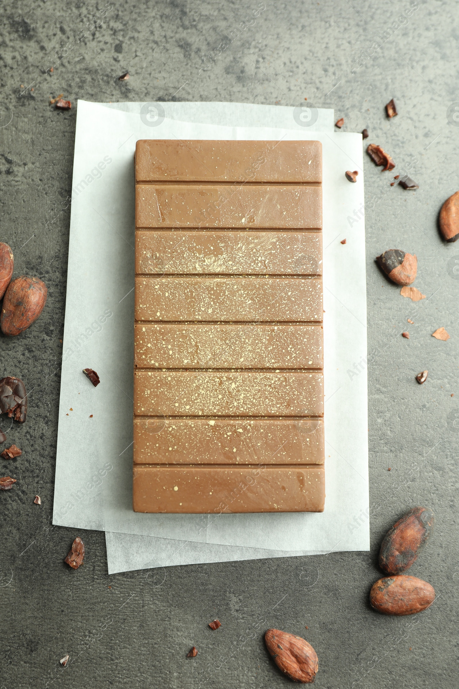 Photo of Tasty Dubai chocolate with pistachio, knafeh and cocoa beans on grey textured table, flat lay