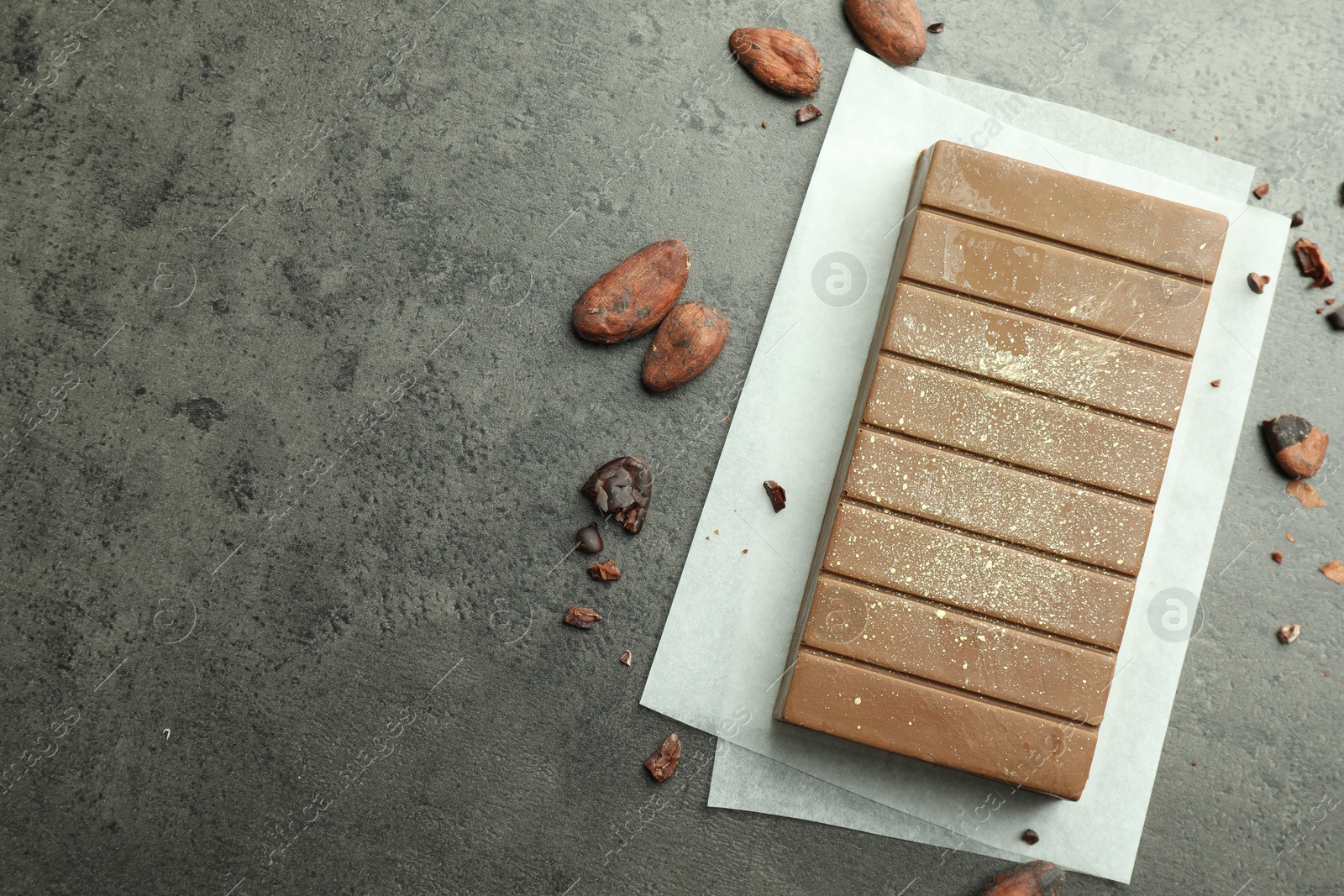 Photo of Tasty Dubai chocolate with pistachio, knafeh and cocoa beans on grey textured table, flat lay. Space for text