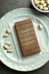 Photo of Tasty Dubai chocolate with pistachios and knafeh on grey textured table, flat lay