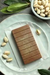 Photo of Tasty Dubai chocolate with pistachios and knafeh on grey textured table, flat lay