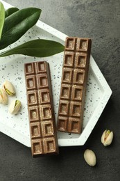 Photo of Tasty Dubai chocolate with pistachios and knafeh on grey textured table, flat lay