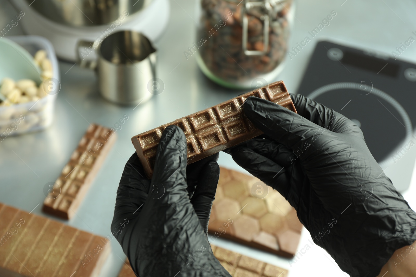 Photo of Woman holding tasty Dubai chocolate with pistachios and knafeh at grey table, closeup