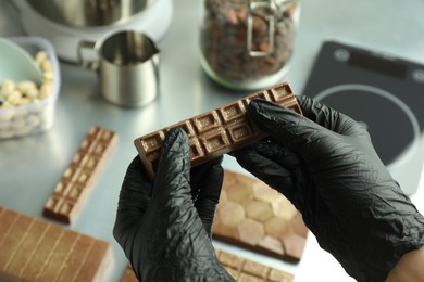 Photo of Woman holding tasty Dubai chocolate with pistachios and knafeh at grey table, closeup