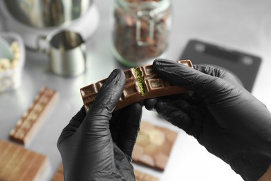 Photo of Woman breaking tasty Dubai chocolate with pistachios and knafeh on blurred background, closeup