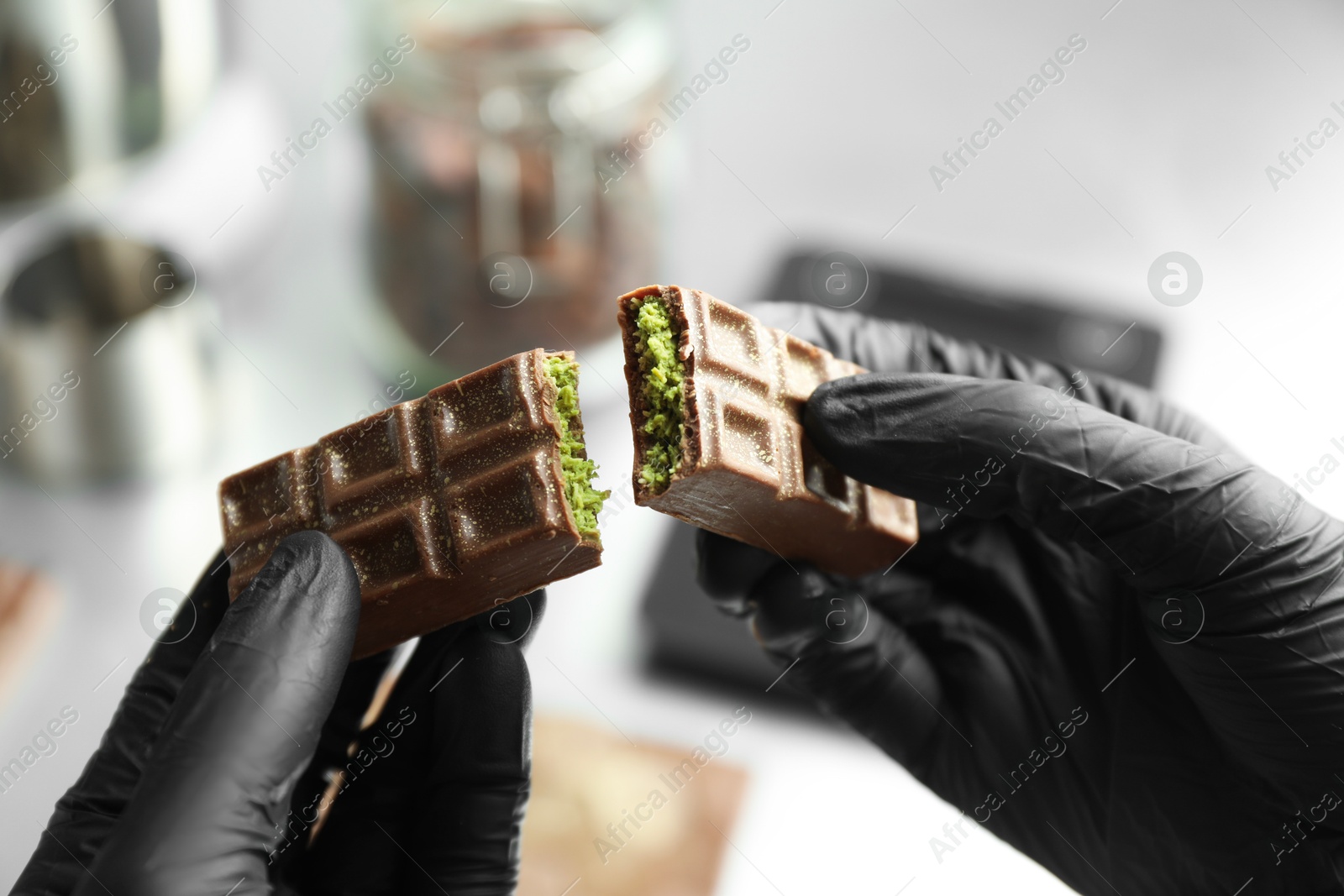 Photo of Woman breaking tasty Dubai chocolate with pistachios and knafeh on blurred background, closeup