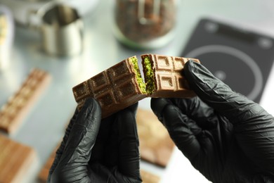 Woman breaking tasty Dubai chocolate with pistachios and knafeh at grey table, closeup