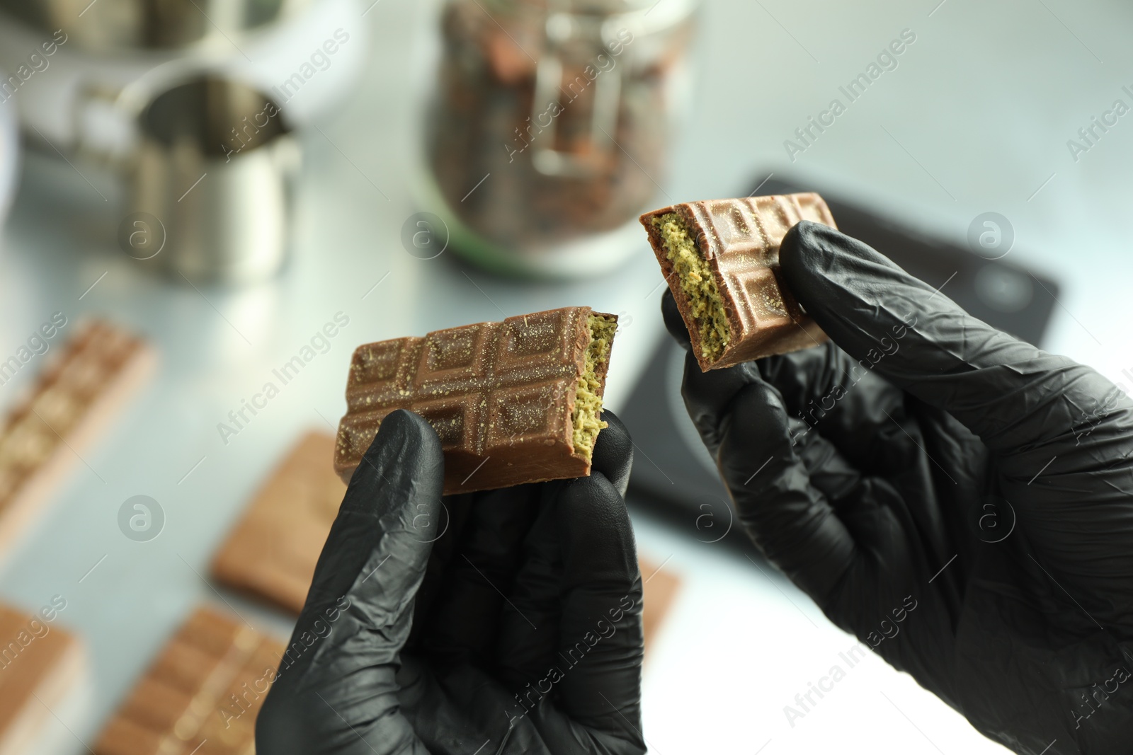 Photo of Woman holding pieces of tasty Dubai chocolate with pistachios and knafeh at grey table, closeup
