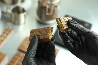 Photo of Woman holding pieces of tasty Dubai chocolate with pistachios and knafeh at grey table, closeup