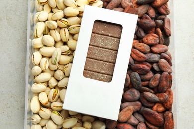 Photo of Tasty Dubai chocolate bar with knafeh in package, pistachios and cocoa beans on textured table, top view. Space for text