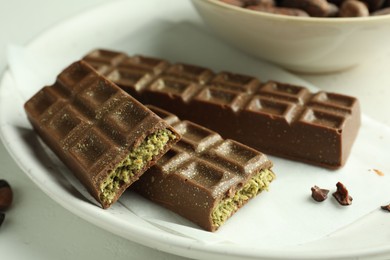 Photo of Tasty Dubai chocolate bars with pistachios and knafeh on light table, closeup