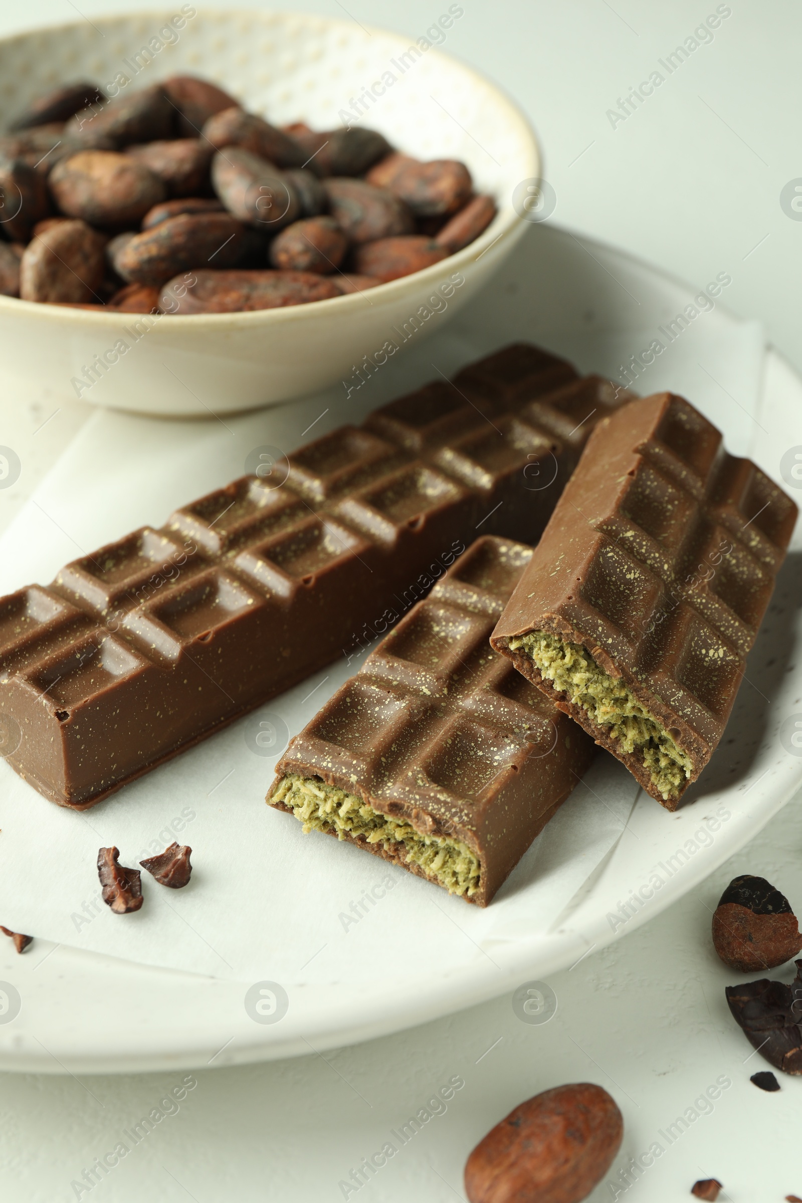 Photo of Tasty Dubai chocolate bars with pistachios, knafeh and cocoa beans on light table, closeup