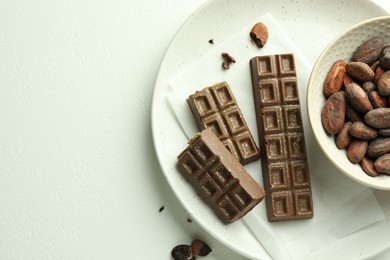 Photo of Tasty Dubai chocolate bars with pistachios, knafeh and cocoa beans on white textured table, top view. Space for text