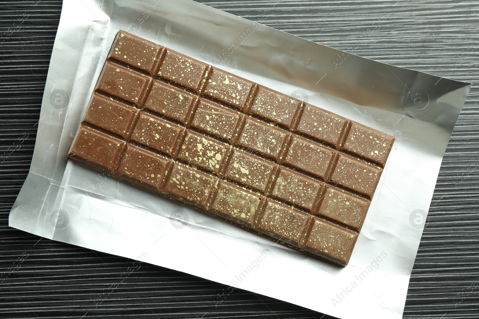 Photo of One tasty Dubai chocolate bar with pistachios and knafeh on black wooden table, top view