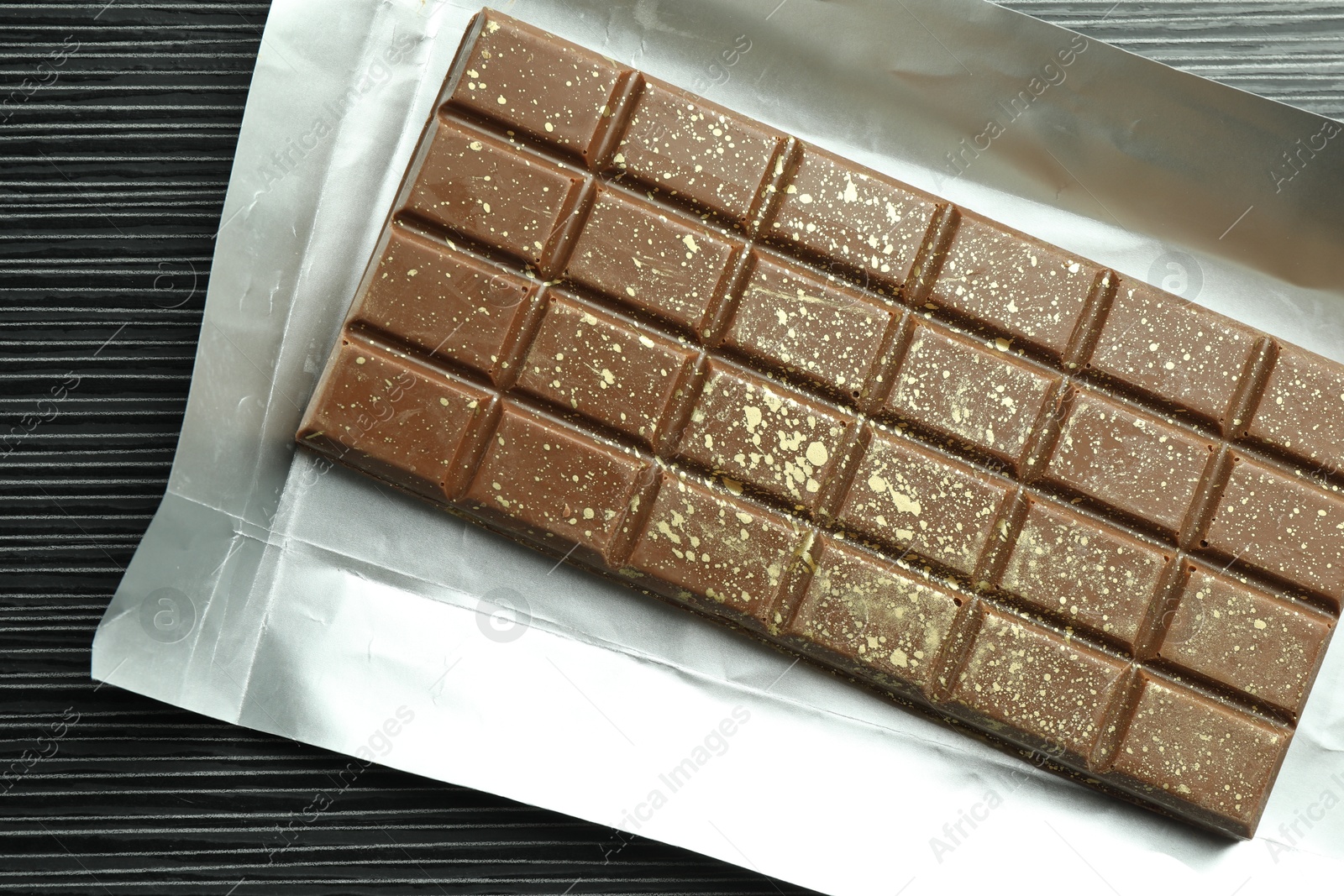 Photo of One tasty Dubai chocolate bar with pistachios and knafeh on black wooden table, top view