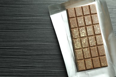 Photo of One tasty Dubai chocolate bar with pistachios and knafeh on black wooden table, top view. Space for text