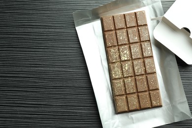 Photo of One tasty Dubai chocolate bar with pistachios and knafeh on black wooden table, top view. Space for text