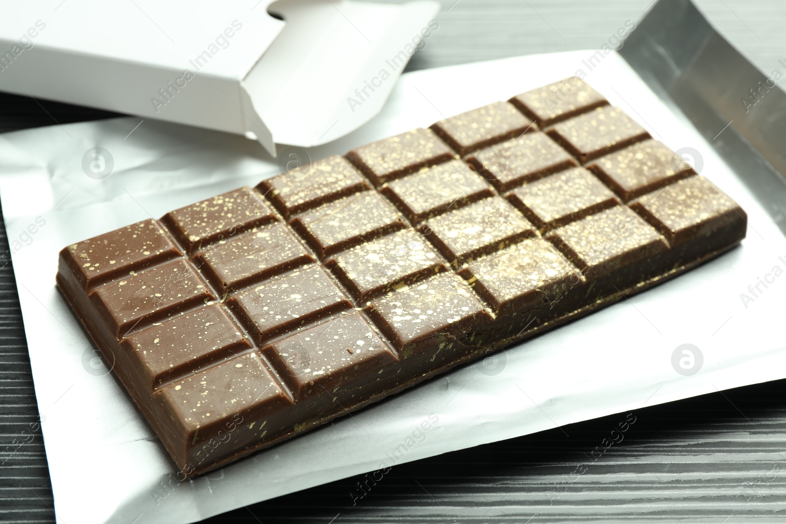 Photo of One tasty Dubai chocolate bar with pistachios and knafeh on black wooden table, closeup