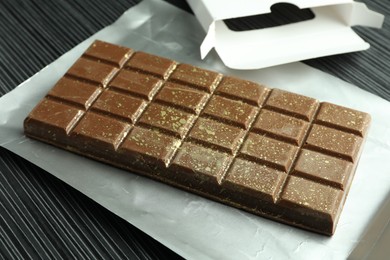 Photo of One tasty Dubai chocolate bar with pistachios and knafeh on black wooden table, closeup