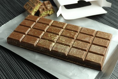 Photo of One tasty Dubai chocolate bar with pistachios and knafeh on black wooden table, closeup