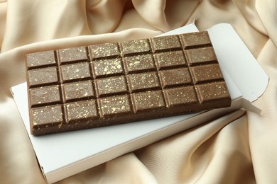 Photo of Tasty Dubai chocolate bar with pistachios, knafeh and package on beige cloth, closeup