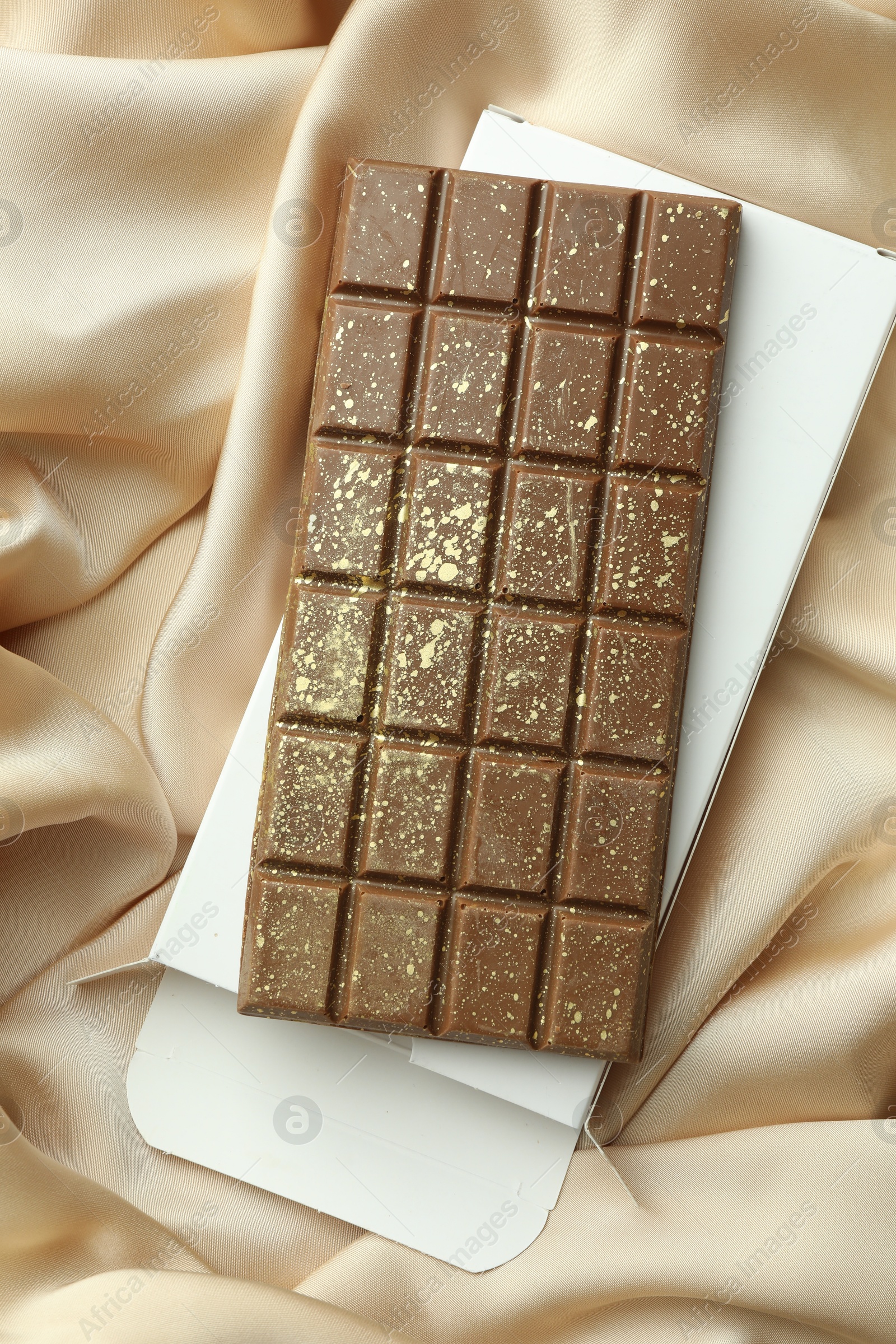 Photo of Tasty Dubai chocolate bar with pistachios, knafeh and package on beige cloth, top view