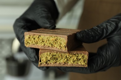 Photo of Woman holding pieces of tasty Dubai chocolate with pistachios and knafeh indoors, closeup