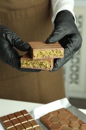 Photo of Woman holding pieces of tasty Dubai chocolate with pistachios and knafeh at table indoors, closeup