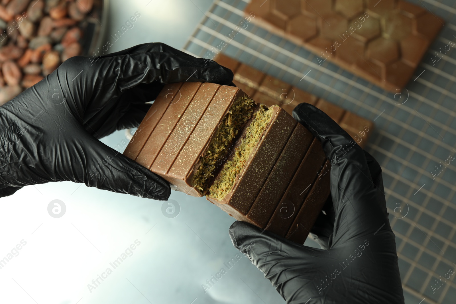 Photo of Woman breaking tasty Dubai chocolate with pistachios and knafeh at grey table, above view