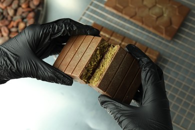 Woman breaking tasty Dubai chocolate with pistachios and knafeh at grey table, above view