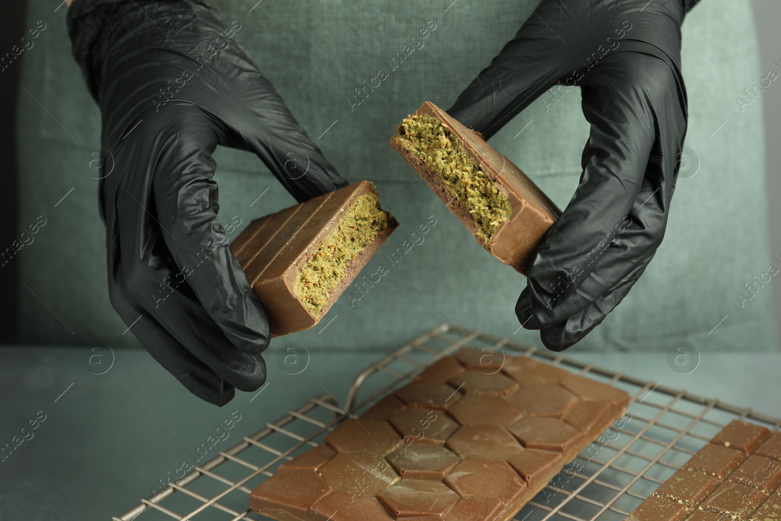 Photo of Woman breaking tasty Dubai chocolate with pistachios and knafeh at grey table, closeup