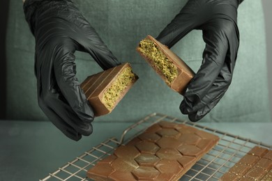 Photo of Woman breaking tasty Dubai chocolate with pistachios and knafeh at grey table, closeup