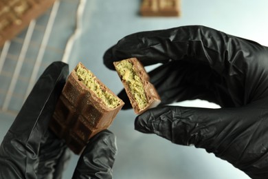 Woman holding pieces of tasty Dubai chocolate with pistachios and knafeh at grey table, closeup