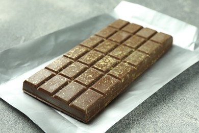 Photo of One tasty Dubai chocolate bar with pistachios and knafeh on grey textured table, closeup