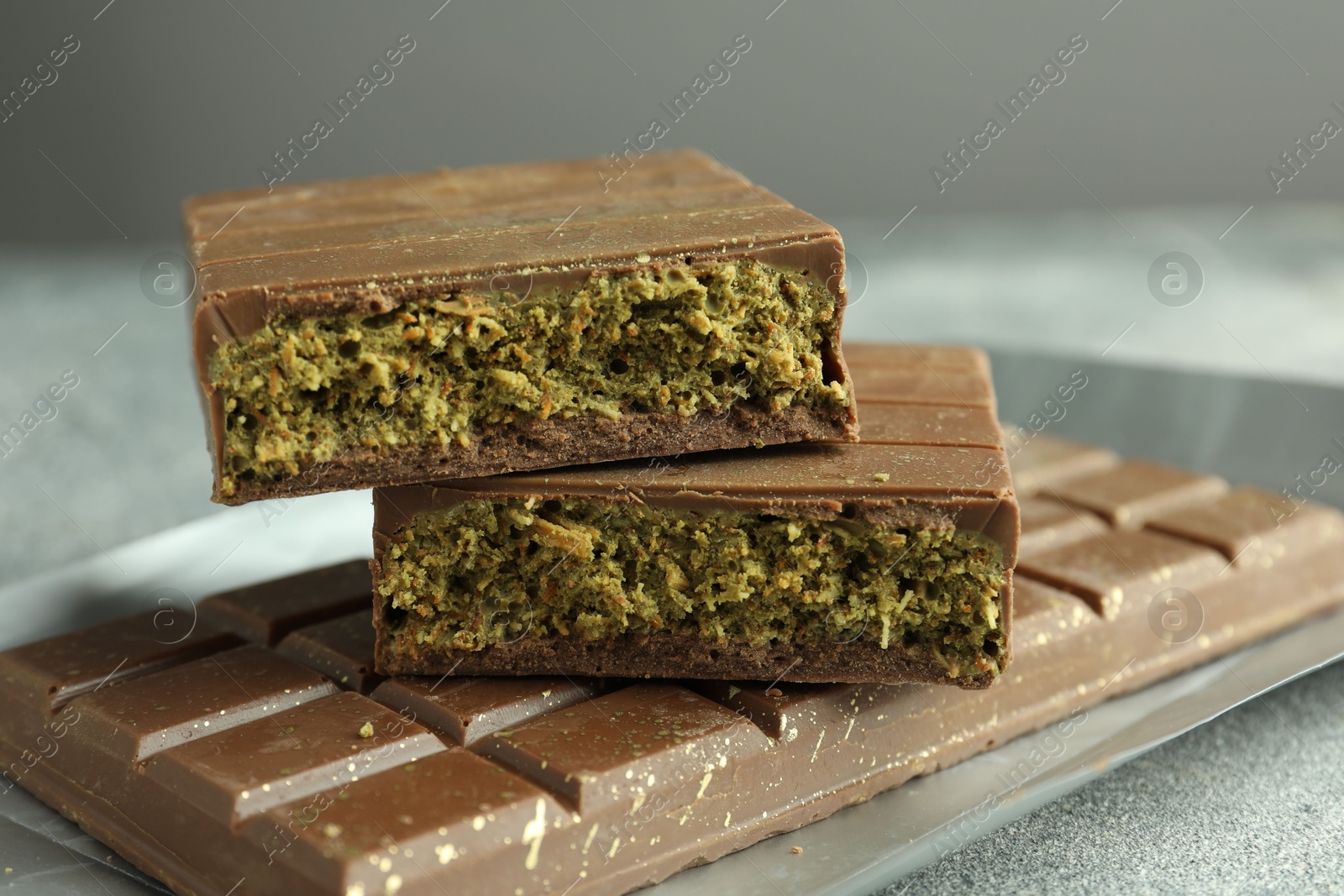 Photo of Tasty Dubai chocolate with pistachios and knafeh on grey textured table, closeup