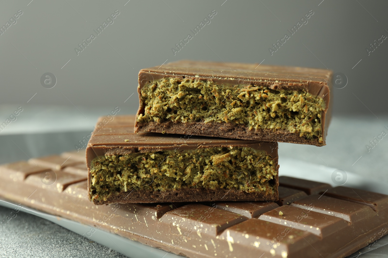 Photo of Tasty Dubai chocolate with pistachios and knafeh on grey textured table, closeup