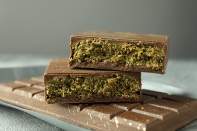 Photo of Tasty Dubai chocolate with pistachios and knafeh on grey textured table, closeup