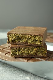 Photo of Tasty Dubai chocolate with pistachios and knafeh on grey textured table, closeup