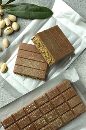 Photo of Tasty Dubai chocolate with pistachios and knafeh on grey textured table, flat lay