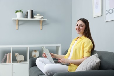 Photo of Young woman using laptop on sofa at home