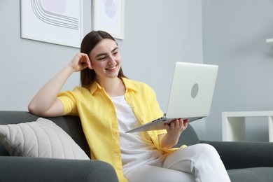 Photo of Happy young woman having video chat via laptop on sofa at home