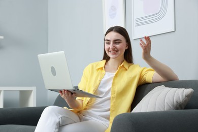 Photo of Happy young woman having video chat via laptop on sofa at home