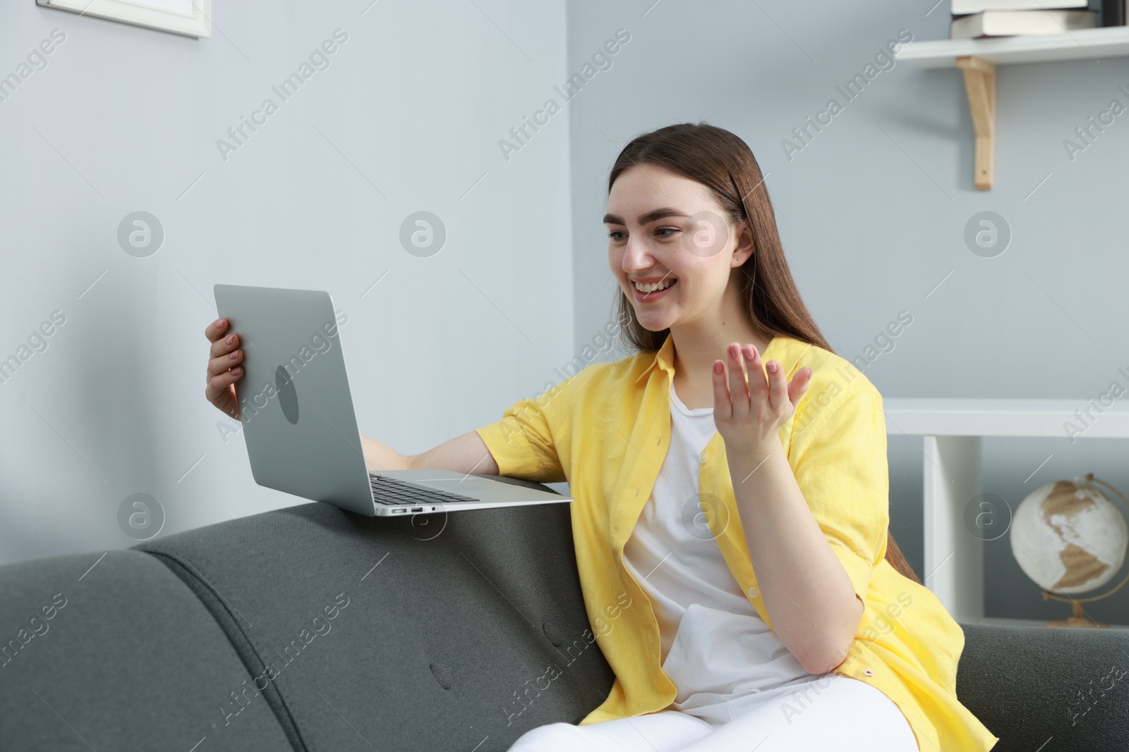 Photo of Happy young woman having video chat via laptop on sofa at home