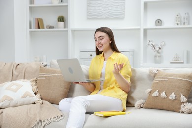 Photo of Happy young woman having video chat via laptop on sofa at home