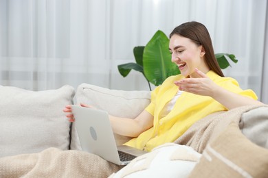 Photo of Happy young woman having video chat via laptop on sofa at home