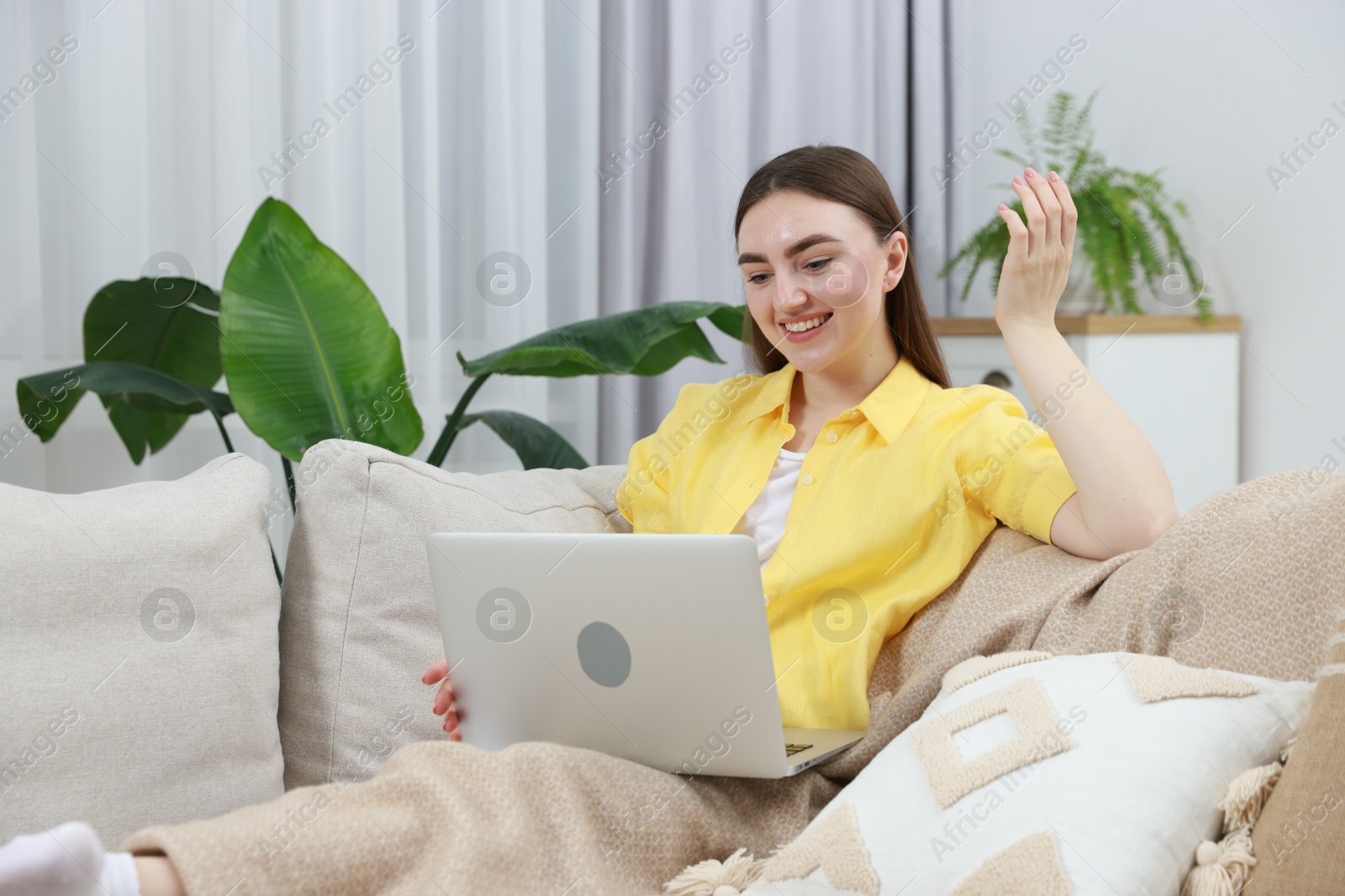 Photo of Happy young woman having video chat via laptop on sofa at home