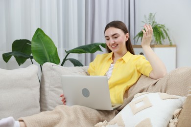 Photo of Happy young woman having video chat via laptop on sofa at home