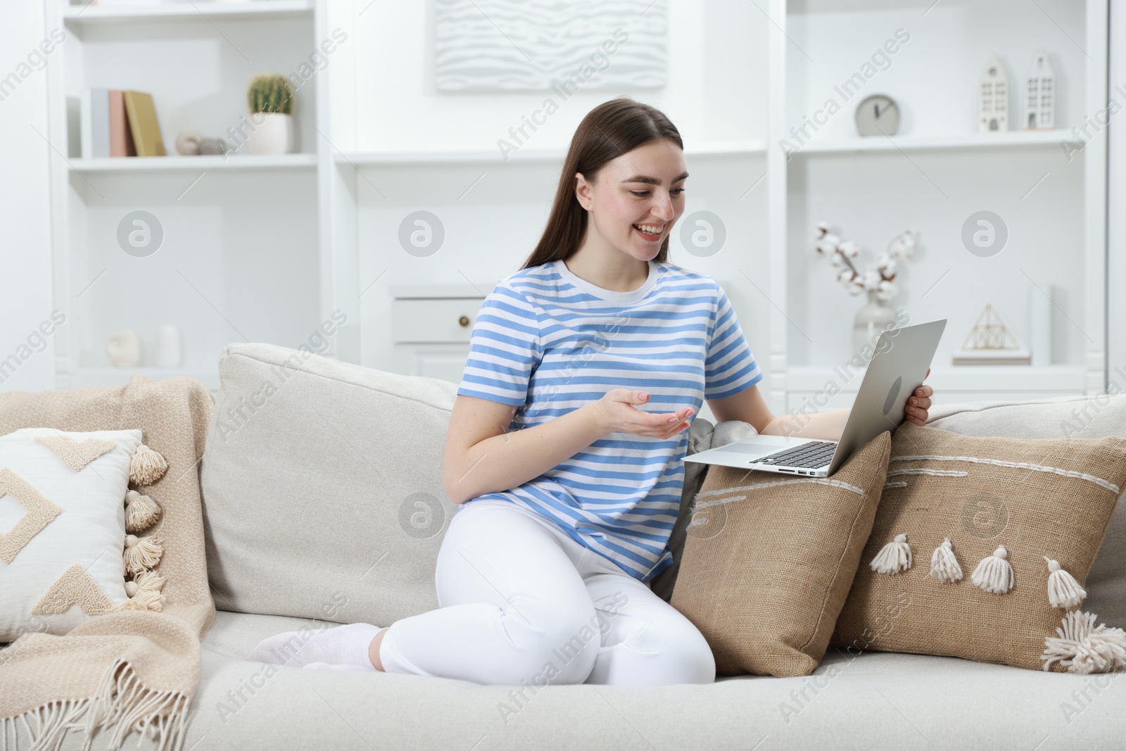 Photo of Happy young woman having video chat via laptop on sofa at home