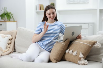 Photo of Happy young woman having video chat via laptop on sofa at home