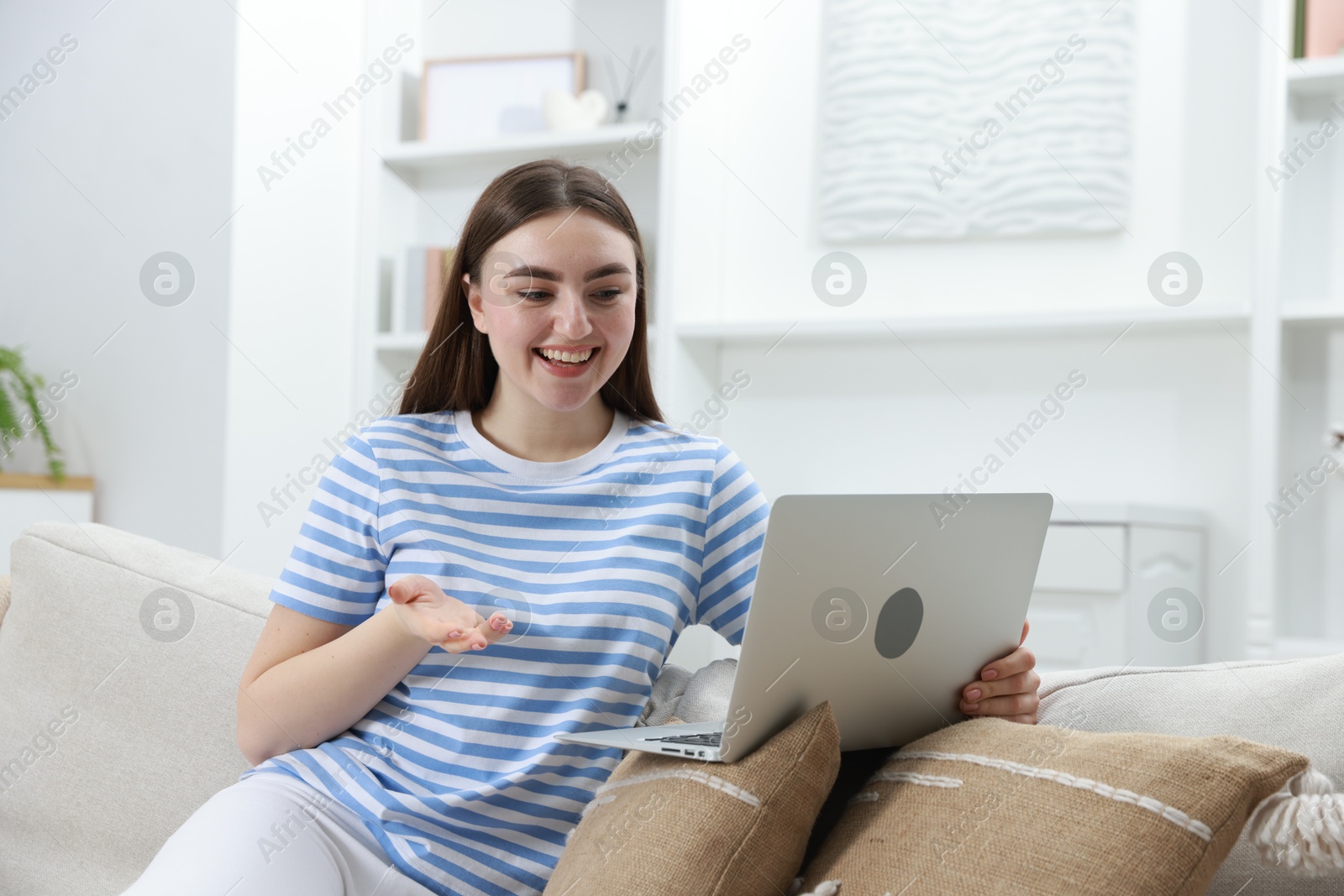 Photo of Happy young woman having video chat via laptop on sofa at home